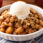 Warm homemade microwave apple crisp topped with vanilla ice cream in a white serving dish on a wooden table.
